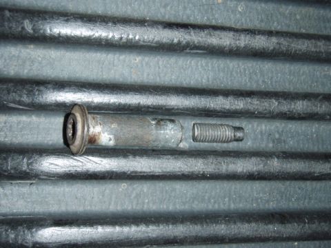 1995 Ford F-150 - A broken bolt and its threaded stud lie on a dark, ribbed surface.