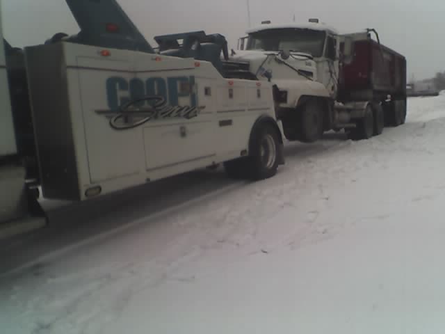Tow truck with 'COOPER' logo towing a dump truck in the snow