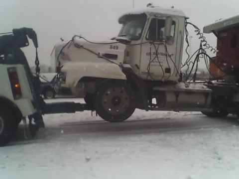 1992 Ford Bronco - A tow truck is towing a semi-truck in the snow. The semi-truck has text on its door.