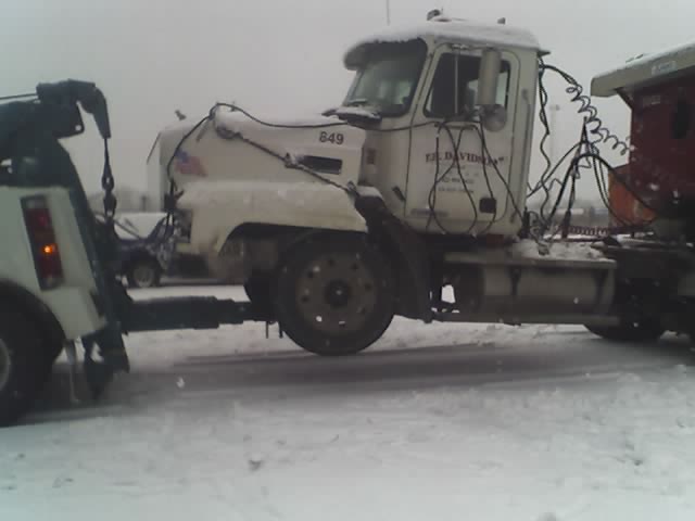 Tow truck hooking up to a white semi-truck in snowy conditions. Semi-truck has 'EL. DAVIDSON' text on the door