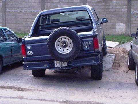 1995 Ford F-150 - A dark blue Ford pickup truck is parked next to another vehicle, showing its rear end and spare tire.