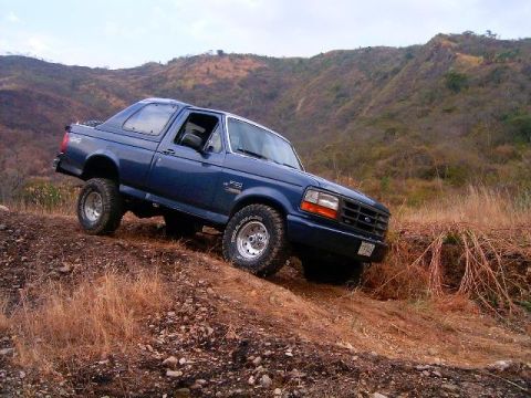 1995 Ford F-150 - A blue Ford F-150 truck navigates a steep, dry, grassy hill in a rural, mountainous area.