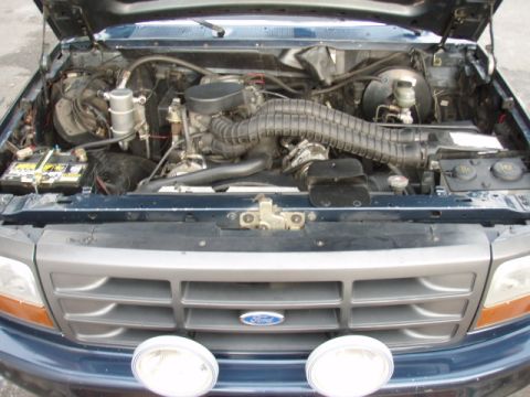 1995 Ford F-150 - The engine compartment of a dark blue Ford F-150 truck is displayed with the hood raised.