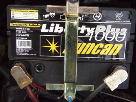 1995 Ford F-150 - Close-up of a car battery, showing its brand name and specifications, with visible terminals and a metal securing bracket.