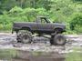 2004 Jeep Wrangler - Lifted pickup truck with oversized tires navigates a muddy terrain.