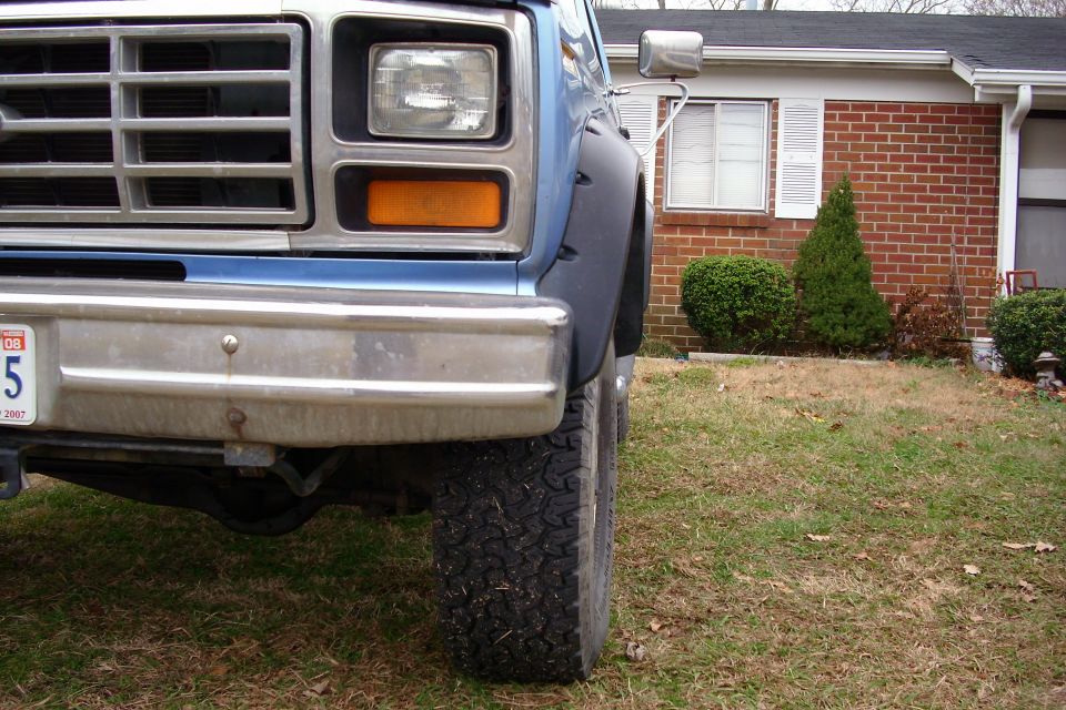 Front corner of a blue and silver two-tone truck parked by a brick house