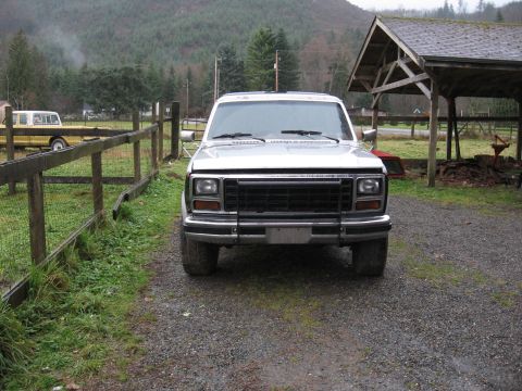 1984 Ford Bronco - Silver 1980s Ford pickup truck parked in a rural setting with a wooden fence and barn structure.