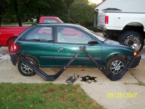 1979 Ford F-250 - Leaf springs are laid out in front of a green hatchback parked on a driveway, with other trucks visible.