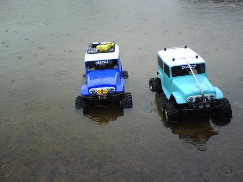 1996 Ford Bronco - Two remote control trucks, one blue and one light blue, are parked in shallow water, with "VARCOR" visible on their windshields.