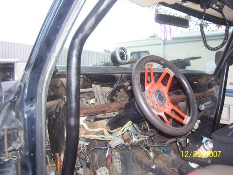 1978 Ford Bronco - The interior of a vehicle shows an aftermarket steering wheel and a prominent roll cage, with exposed wiring visible.