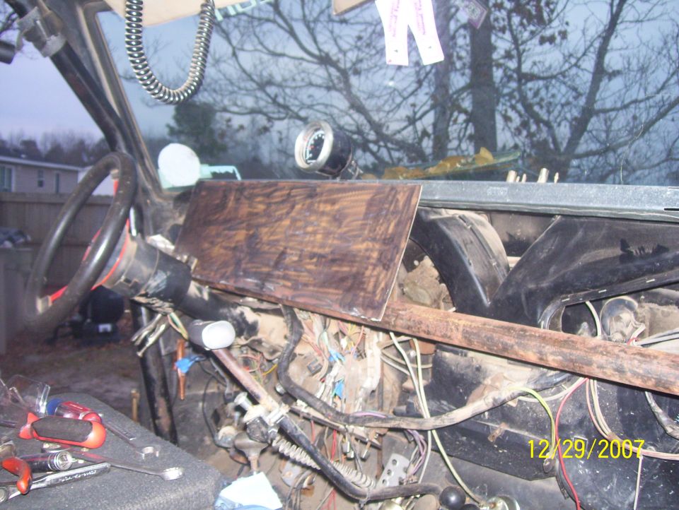 View of a vehicle's dashboard area with exposed wires and tools. A wooden panel is temporarily covering part of the dash
