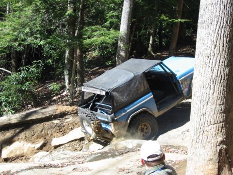 1976 Ford Bronco - This off-road vehicle navigates a challenging, rocky terrain on a wooded trail.