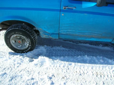 1979 Ford Bronco - A blue SUV's side panel is damaged as it sits in the snow.