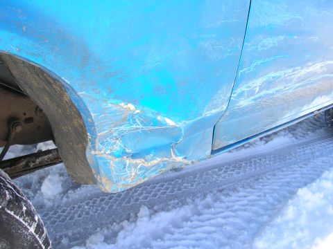 1979 Ford Bronco - Close-up of a dented blue vehicle side panel, partially obscured by snow and mud.
