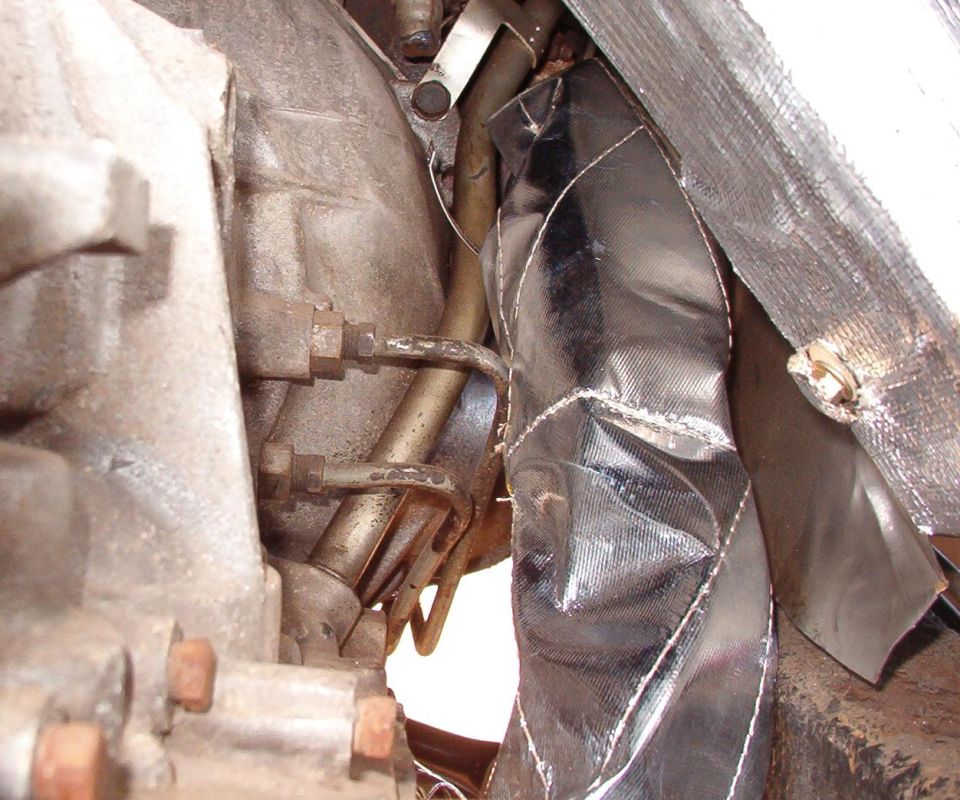 To keep even more heat out, all the exhaust pipes near the body are now wrapped. This stuff smokes & stinks the first few times the engine heats up.   There's also self-adhesive shielding on the body, and that's a stainless heat shield between the body & frame, just R of the wrapped pipe.