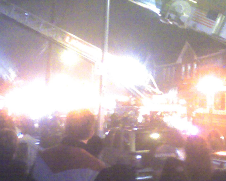 Crowd gathered at an outdoor night event with intense bright lights illuminating the scene
