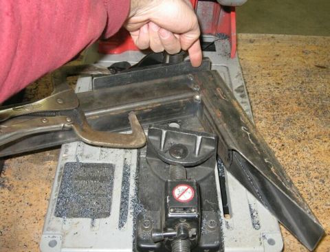 1990 Ford Bronco - A metal bracket is being cut with a metal saw, held in place by clamps and a vise.