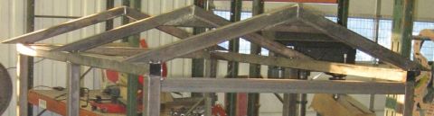 1990 Ford Bronco - A metal structure, possibly a roof truss, is shown in a workshop setting with tools in the background.