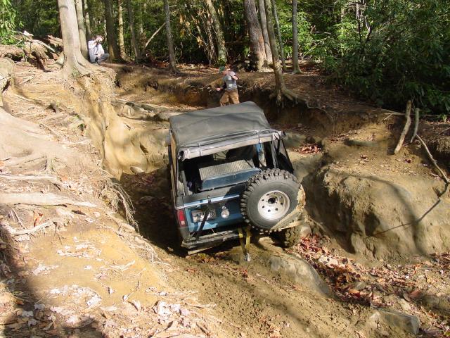 Blue SUV with soft top and spare tire on rear, navigating a muddy, rutted trail