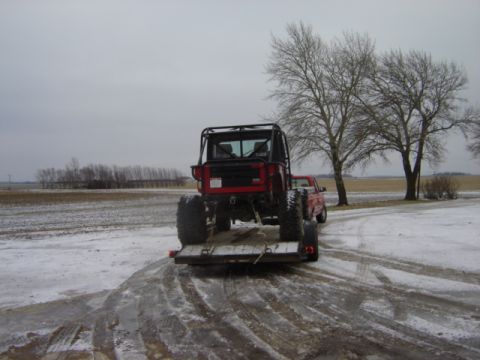 1992 Ford Bronco - Red Jeep on trailer, towed by red pickup truck, in a snowy field with bare trees.