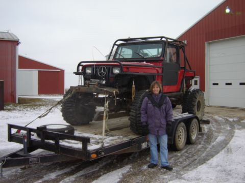 1992 Ford Bronco - A woman stands beside a heavily modified red off-road vehicle loaded onto a trailer in a snowy environment.