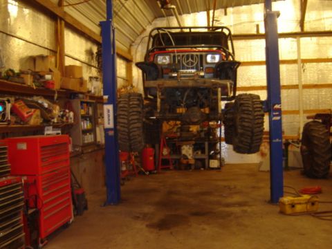 1992 Ford Bronco - An off-road vehicle is suspended on a lift in a garage, revealing its undercarriage and large tires.