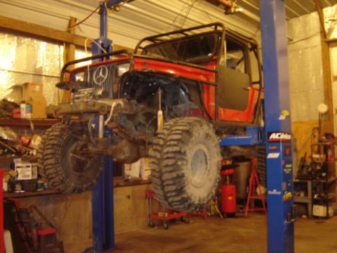 1992 Ford Bronco - A heavily modified Jeep CJ is elevated on a car lift inside a workshop, revealing its large off-road tires.