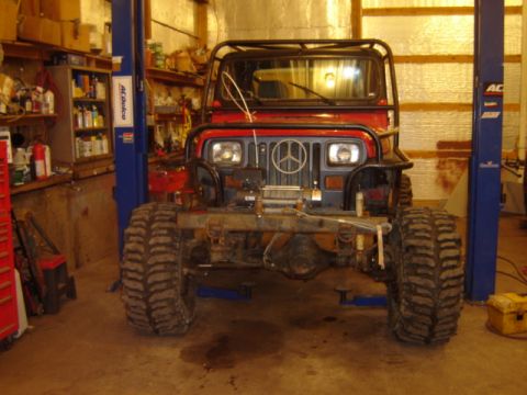 1992 Ford Bronco - A red Jeep Wrangler is elevated on a lift in a garage, equipped with large off-road tires.