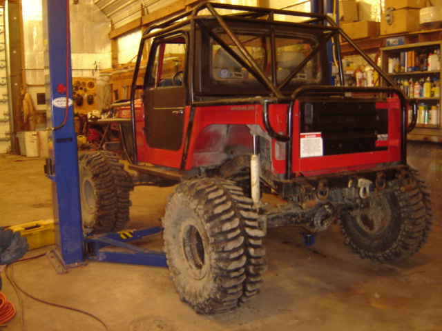 Red off-road vehicle with roll cage and large tires on a lift