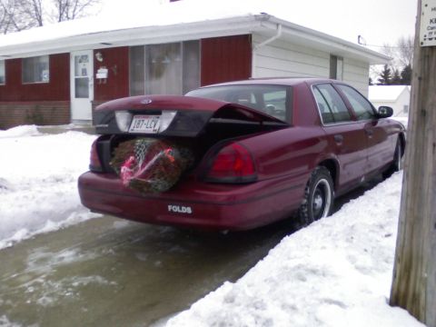 2001 Ford Crown Victoria - A maroon 2001 Ford Crown Victoria is parked in the snow with its trunk open, revealing a wreath inside.