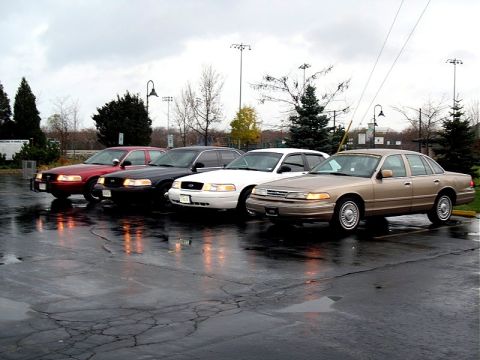 2001 Ford Crown Victoria - Four Ford Crown Victorias are parked in a lot on a cloudy day.