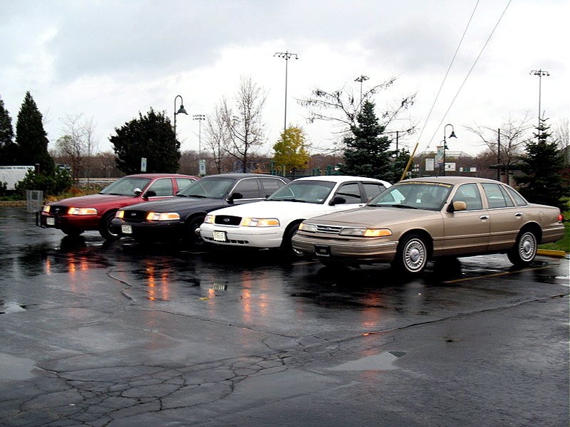 Four 2001 Ford Crown Victorias parked in a wet lot under a cloudy sky