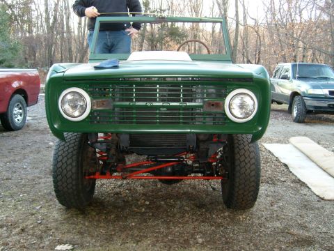 1974 Ford Bronco - Front view of a green 1974 Ford Bronco, its distinctive grille and headlights, with other vehicles visible in the background.
