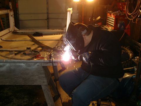 1974 Ford Bronco - A person is welding on a vehicle frame in a workshop setting, with tools and equipment visible.