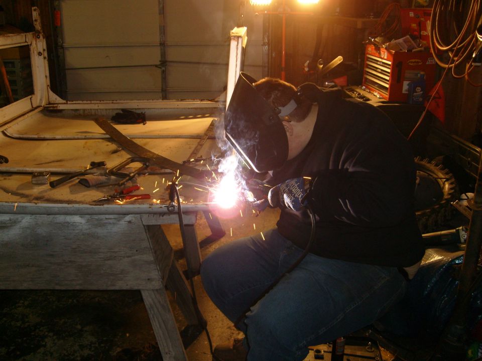 Person welding on the frame of what appears to be an old SUV or truck in a garage