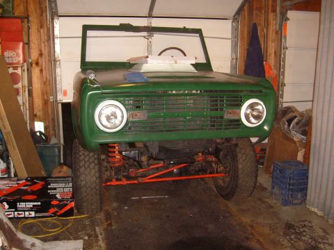 1974 Ford Bronco - The front end of a green Ford Bronco is visible in a garage, with its grille and headlights prominent.