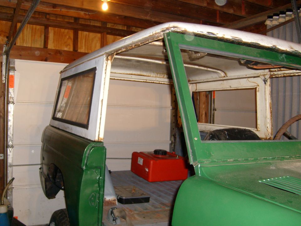 Green 1974 Ford Bronco in a garage, viewed from the side, showing its interior and a red fuel tank
