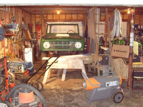 1974 Ford Bronco - A green 1974 Ford Bronco is parked in a cluttered garage, possibly undergoing restoration.