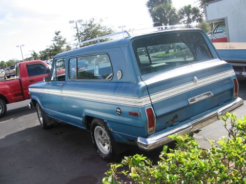 1978 Jeep Cherokee - This blue station wagon has a roof rack and dual side stripes. A red pickup truck is parked to its left.