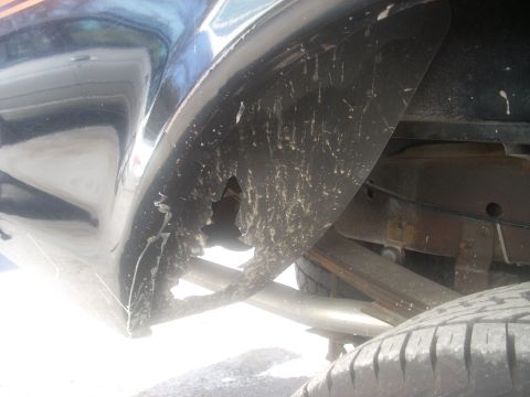 1992 Ford Bronco - Close-up view of the rear wheel well and suspension, showing damage to the liner and visible suspension parts.