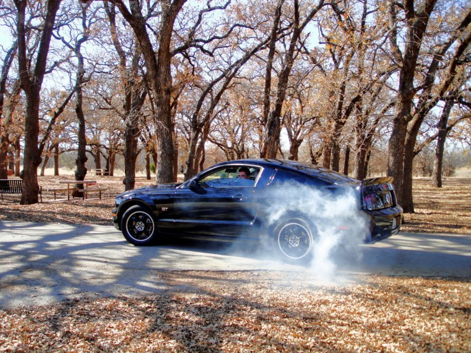 Dark blue Ford Mustang doing a burnout, rear-wheel drive, with smoke billowing
