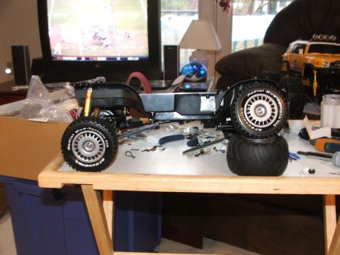 1996 Ford Bronco - RC car chassis and a yellow SUV are on a table with tools, suggesting a hobbyist's workspace.