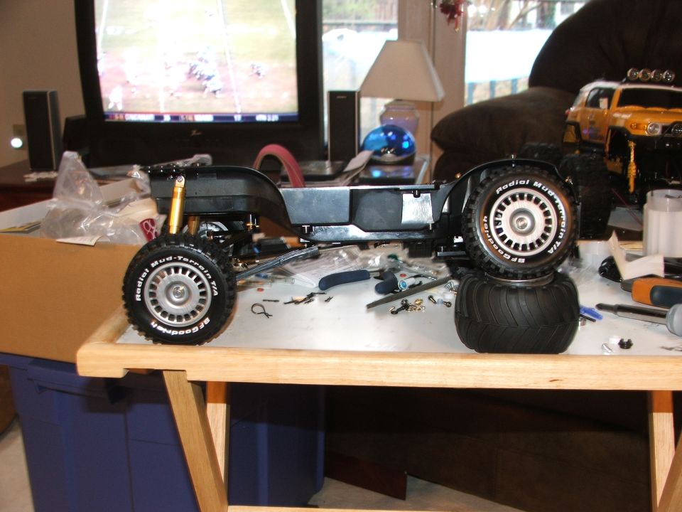 RC car chassis with BFGoodrich Radial Mud-Terrain tires, on a table with tools and a yellow SUV in the background