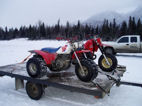 2000 Ford E350 - Two Honda three-wheelers are strapped to a trailer in a snowy landscape, with a pickup truck nearby.