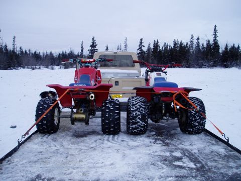 2000 Ford E350 - Two ATVs are strapped to a trailer in a snowy landscape, with a truck visible behind them.