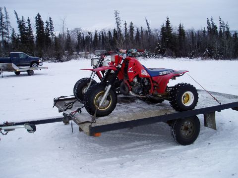 2000 Ford E350 - A red three-wheeled ATV is secured to a trailer in a snowy landscape. The ATV has '250' visible on its fender.