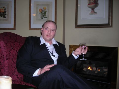 1984 Ford Bronco - Man in a suit holds a glass of red wine while seated in a plush chair next to a fireplace.