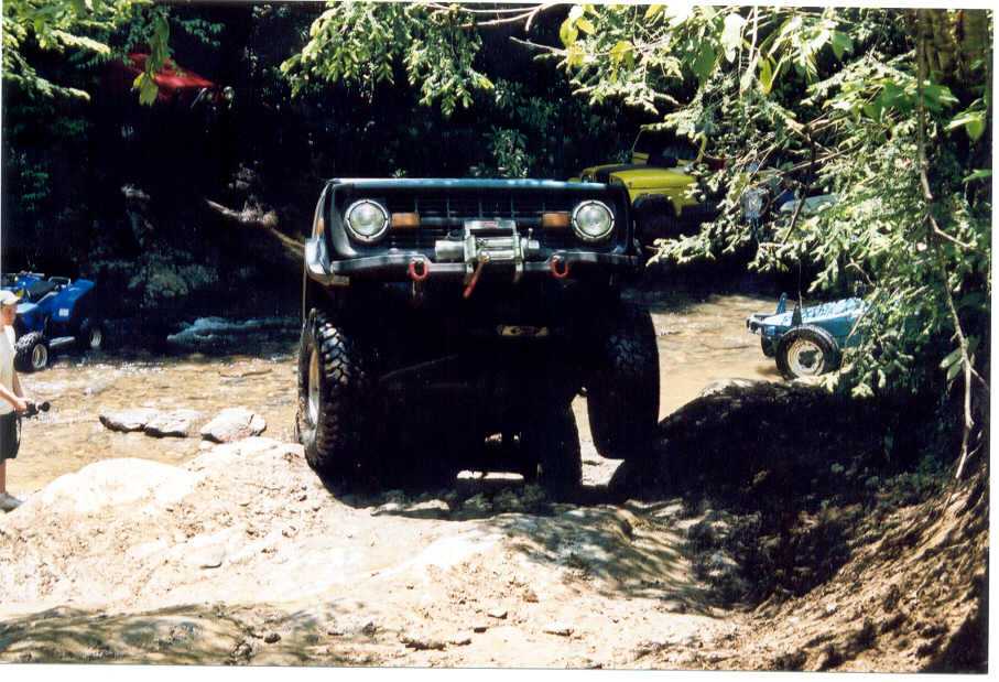 Modified off-road vehicle with winch on rocky terrain. Another ATV and yellow vehicle visible in background