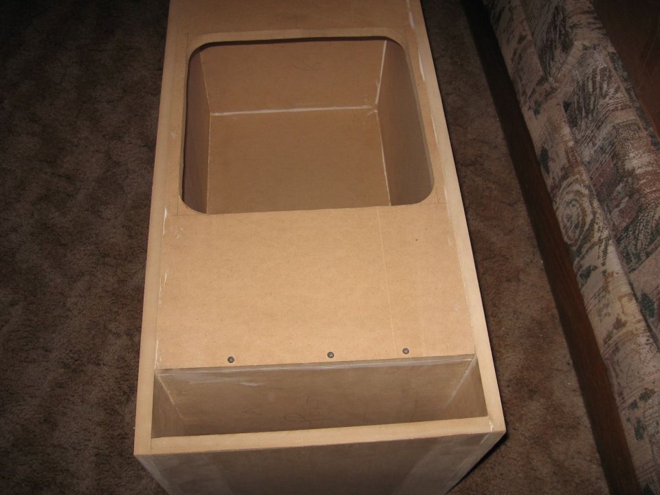 Unfinished MDF speaker box with a large rectangular cutout on top and a smaller open compartment below