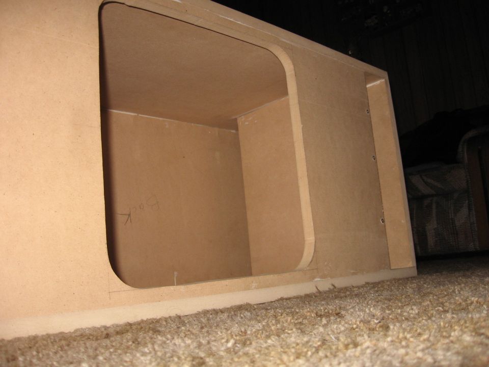 Wood enclosure with two openings, one large rounded and one smaller rectangular. Some writing on the back panel